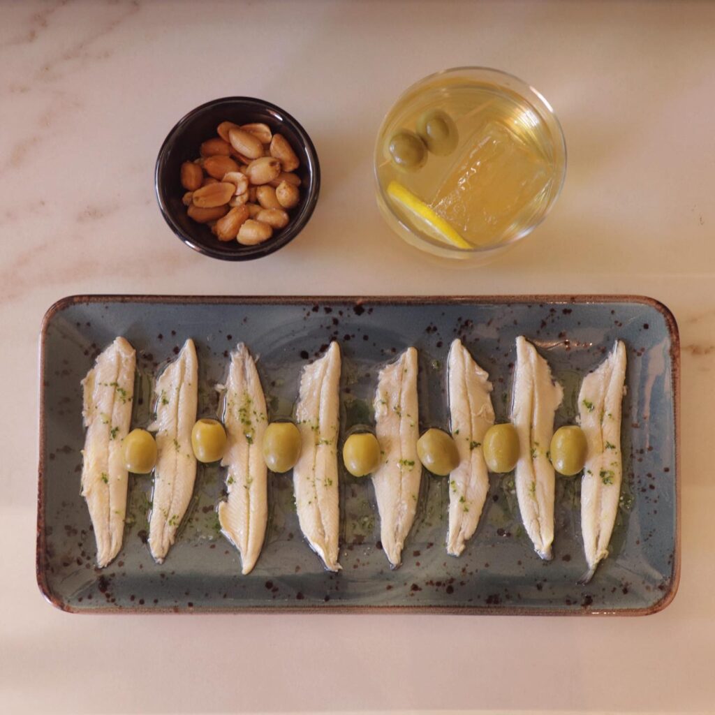Un vermouth acompañado por un plato de boquerones y cacahuetes